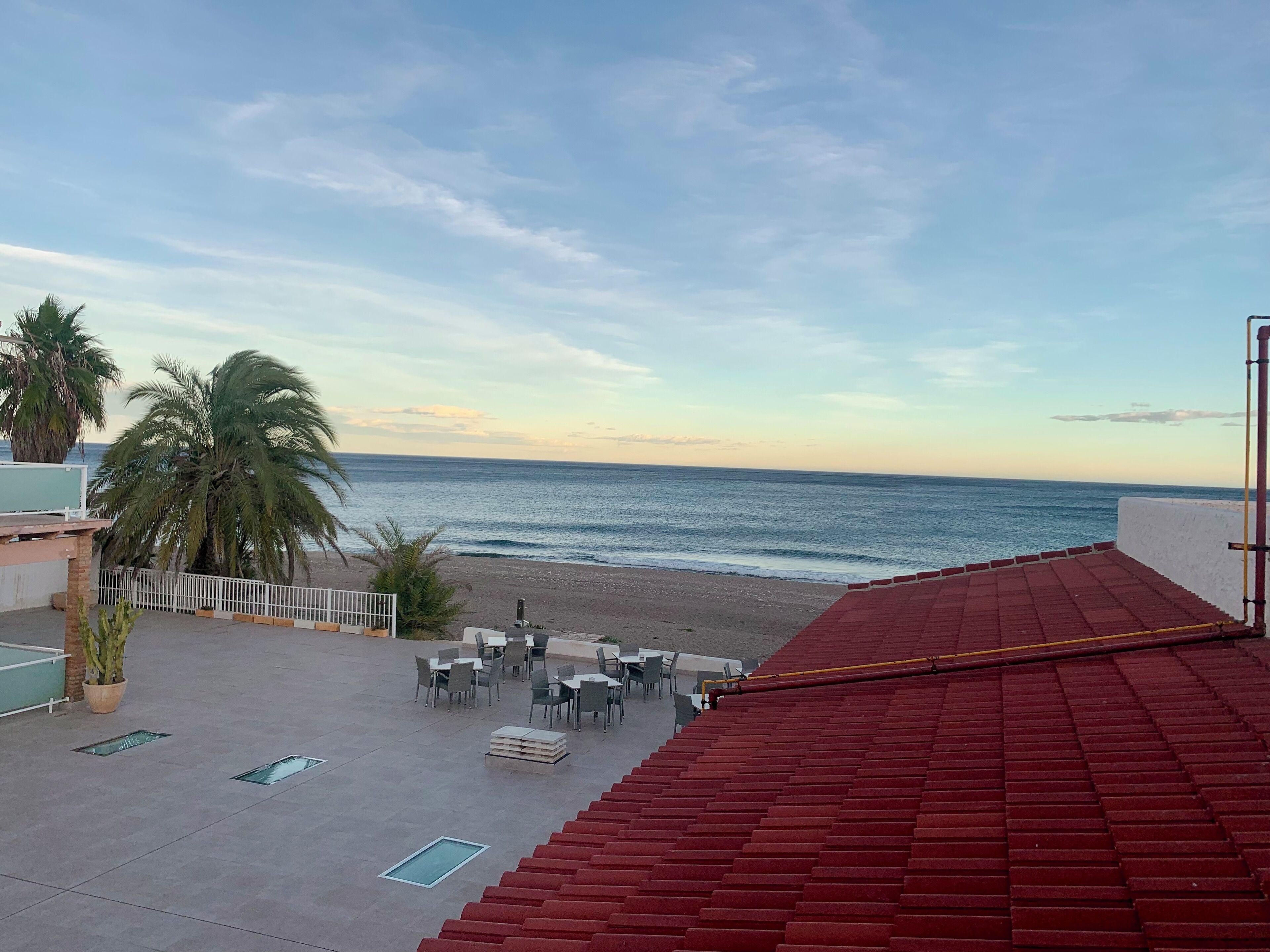 A terrace with red flooring, outdoor seating, and a view of the beach and ocean.