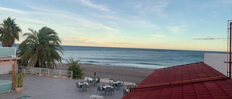A terrace with red flooring, outdoor seating, and a view of the beach and ocean.