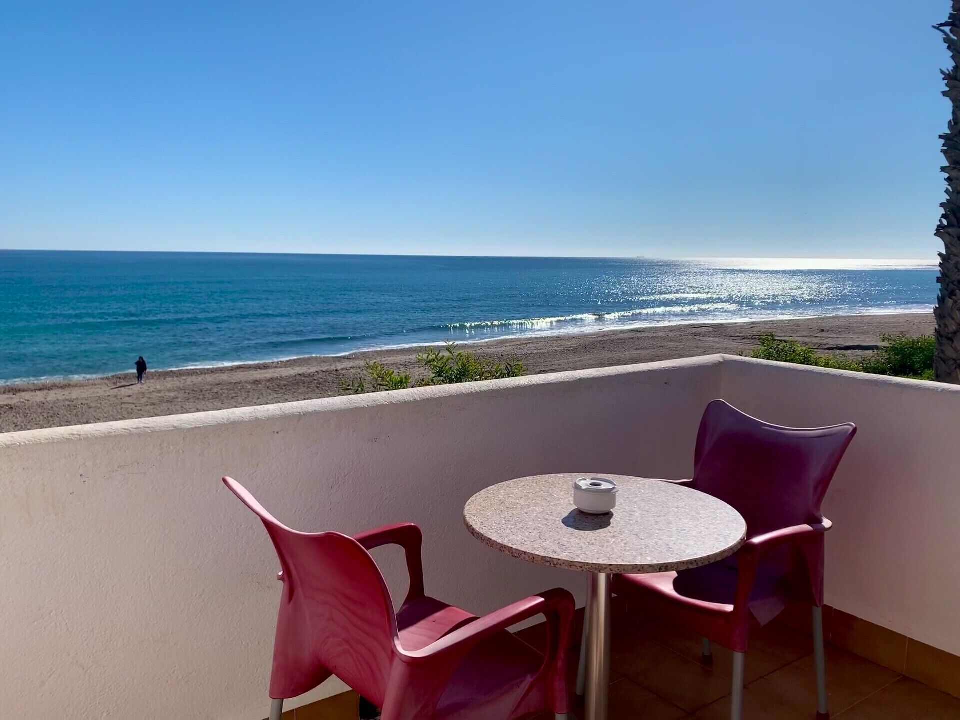 A balcony with a table and chairs overlooking a beach.