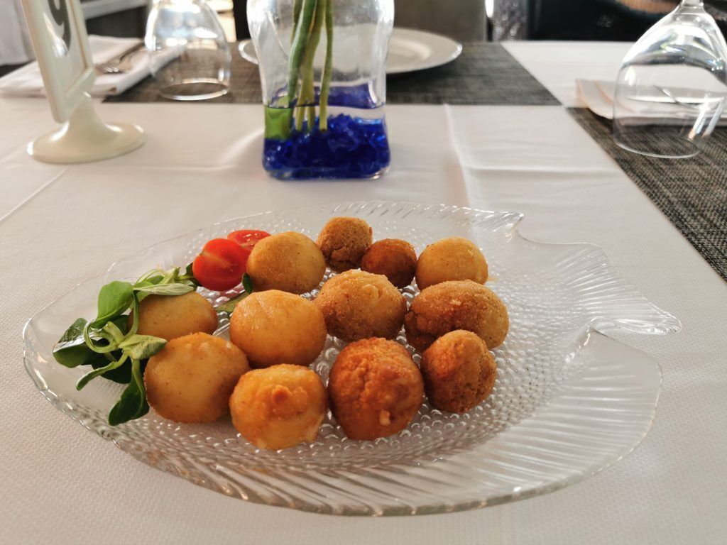 Une table à manger sur laquelle repose une plaque de verre transparent, et qui présente des aliments frits de couleur brun doré, disposés en cercle, peut-être des croquettes, ainsi que quelques éléments de décoration verte.