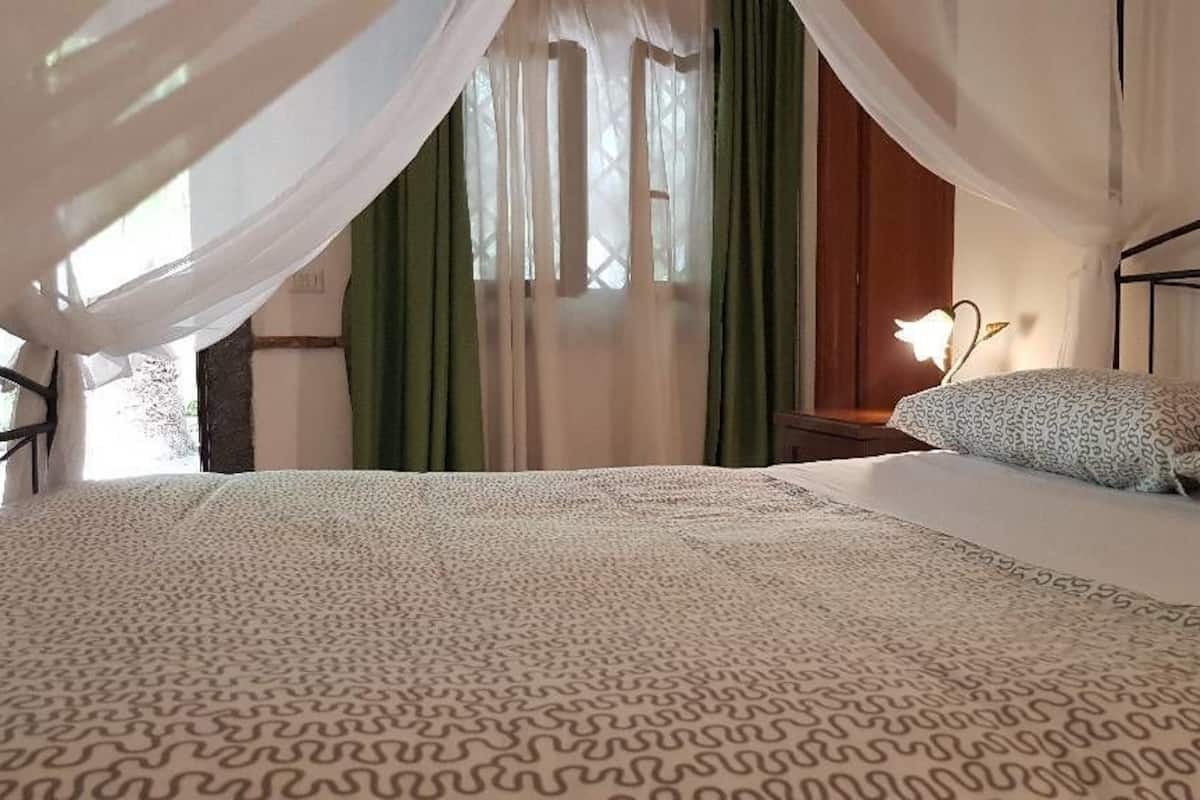 A bedroom with a bed, a nightstand, a lamp, and a window with curtains.