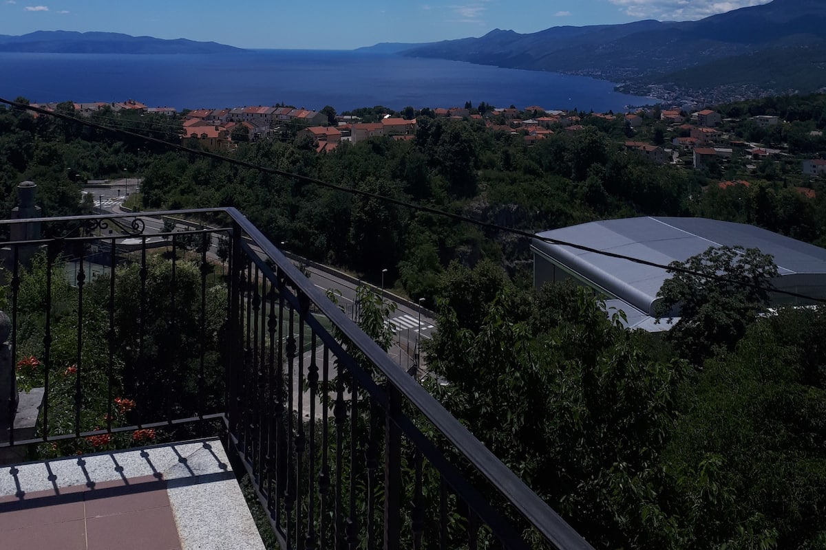 A balcony with a view of a coastal town, mountains, and a clear blue sky.