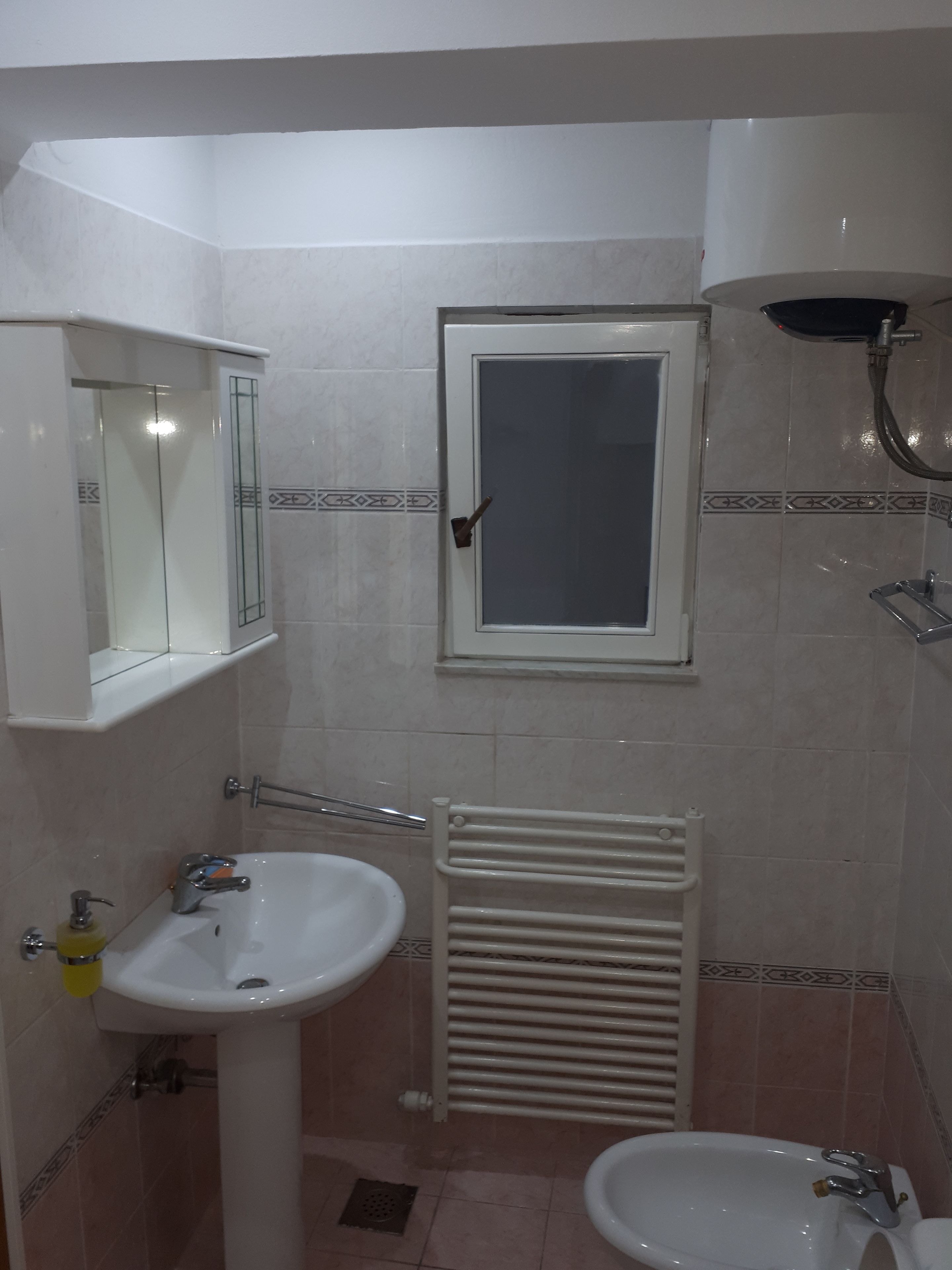 A bathroom with a pedestal sink, a mirror, a window, a shower, and a radiator.