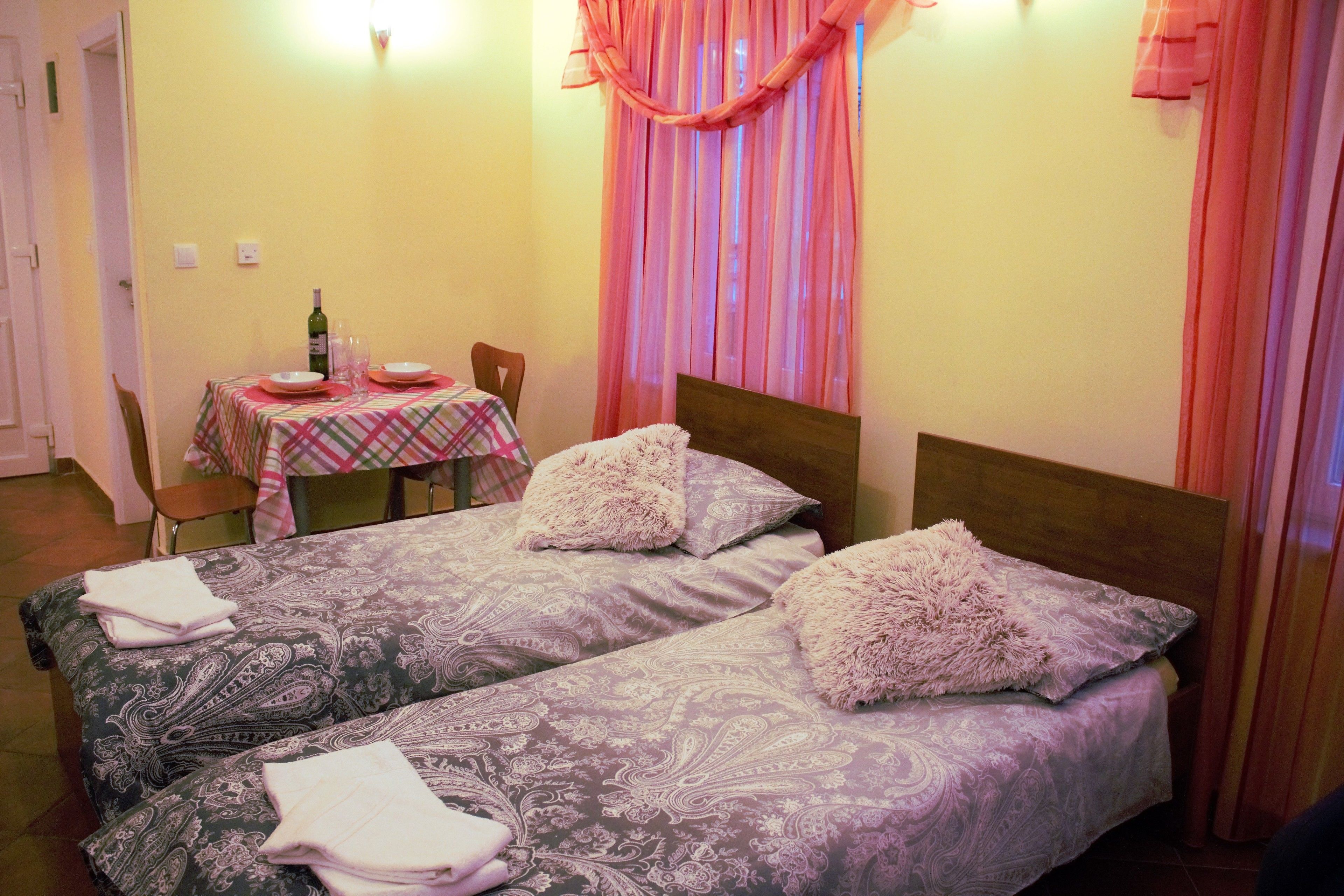 Une chambre avec deux lits, une table sur laquelle se trouvent une bouteille et des verres, et une chaise.