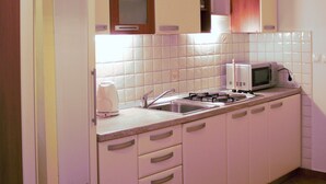 A compact kitchen with white cabinets, a microwave, a stove, and a coffee maker. - Apartments sv. Anton (Kastav)
