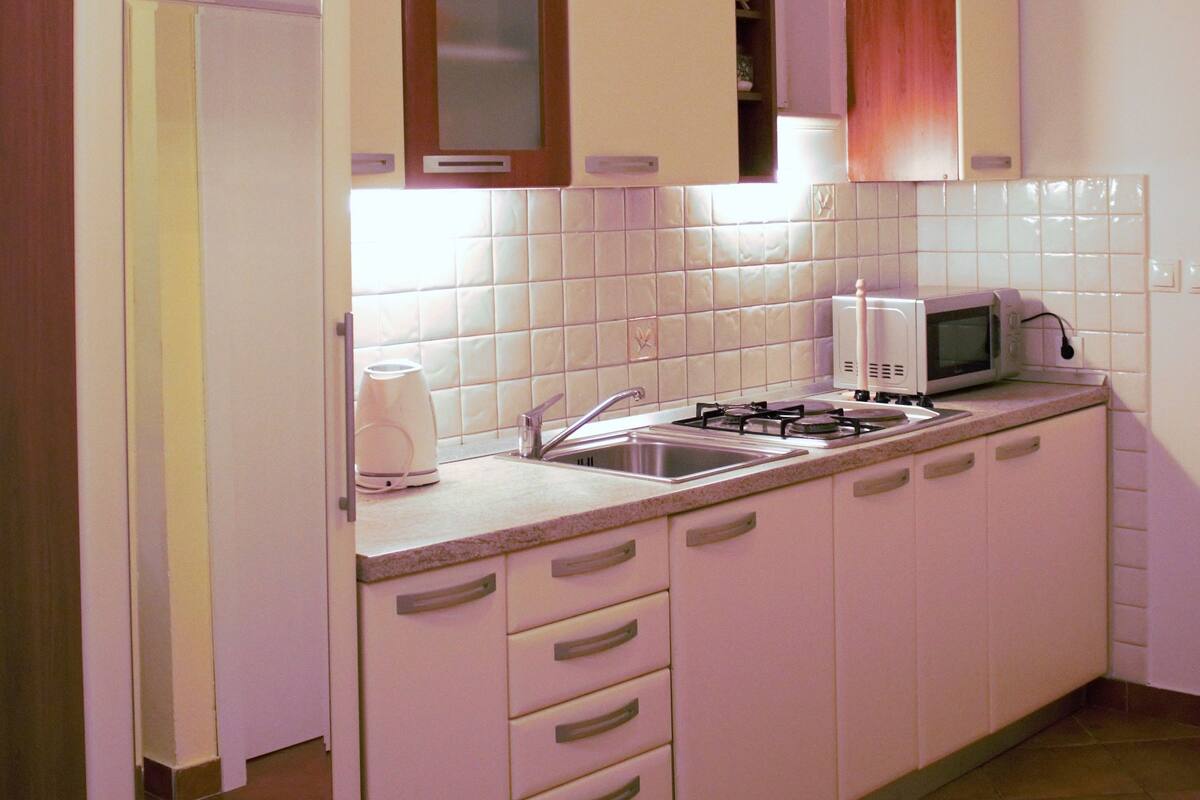 A compact kitchen with white cabinets, a microwave, a stove, and a coffee maker.