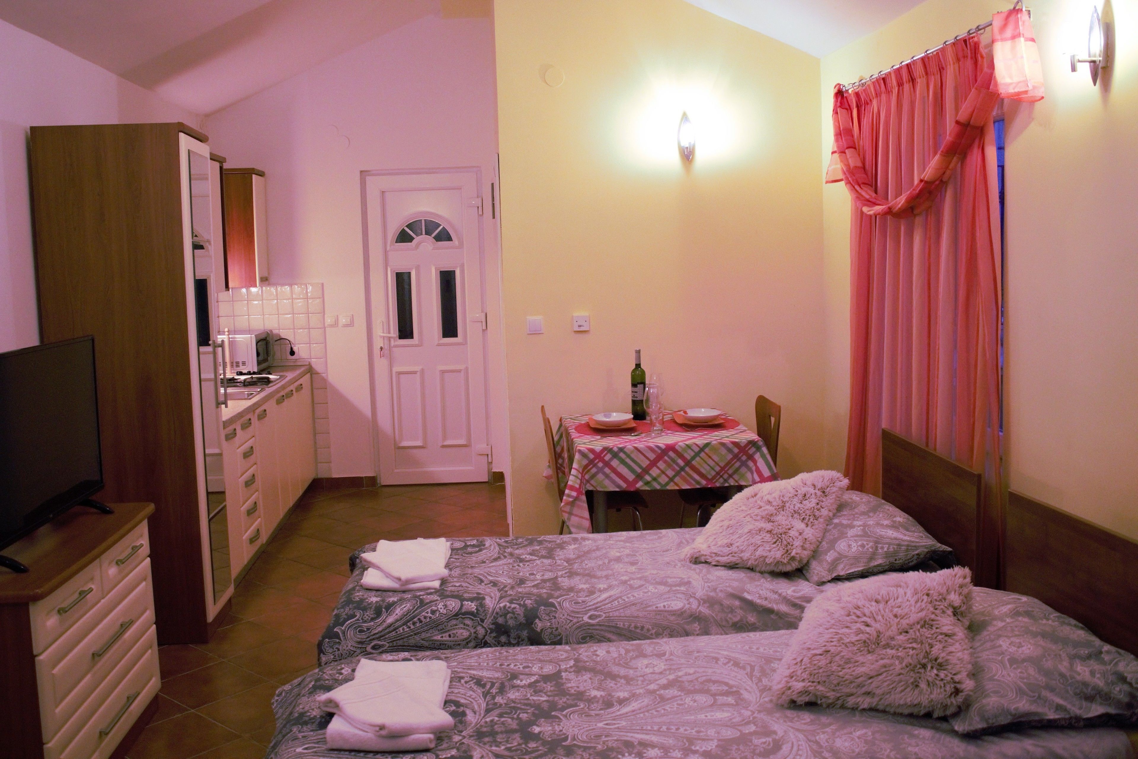 Een slaapkamer met twee bedden, een televisie, een kitchenette en een eettafel.