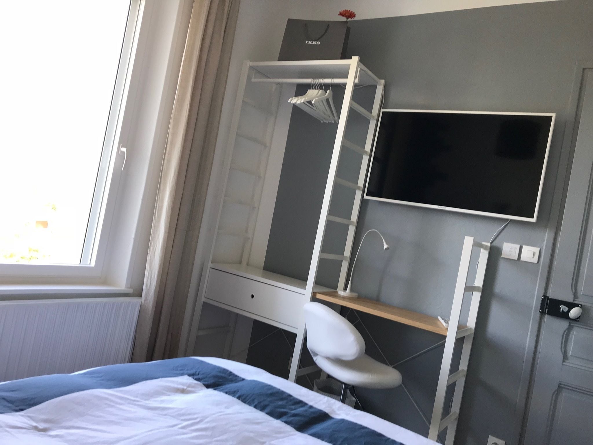 A hotel room with a bed, a desk with a chair, a TV, and a wardrobe.