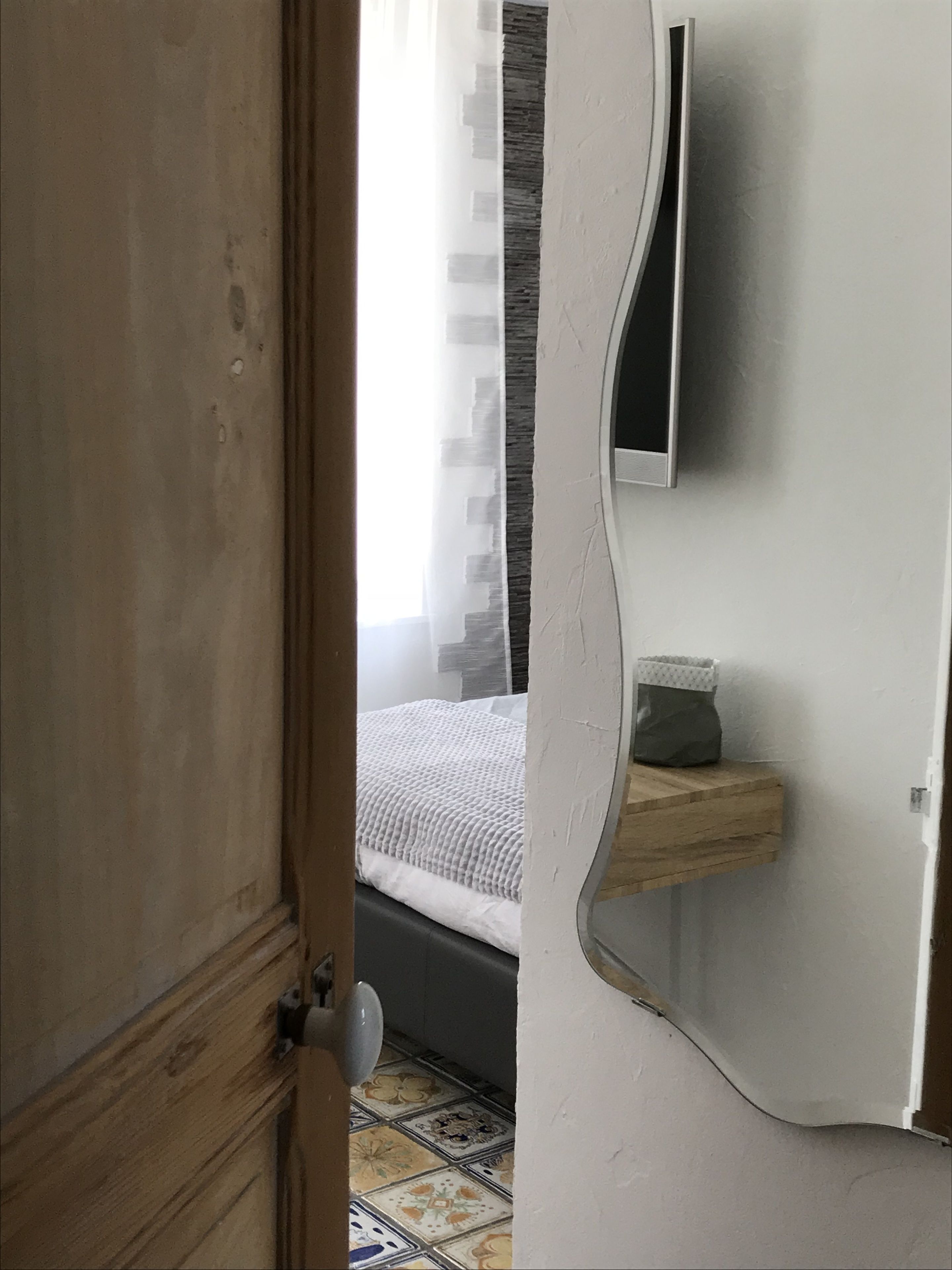 Un dormitorio con cama, mesita de noche, espejo y puerta.
