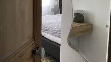 Un dormitorio con cama, mesita de noche, espejo y puerta.