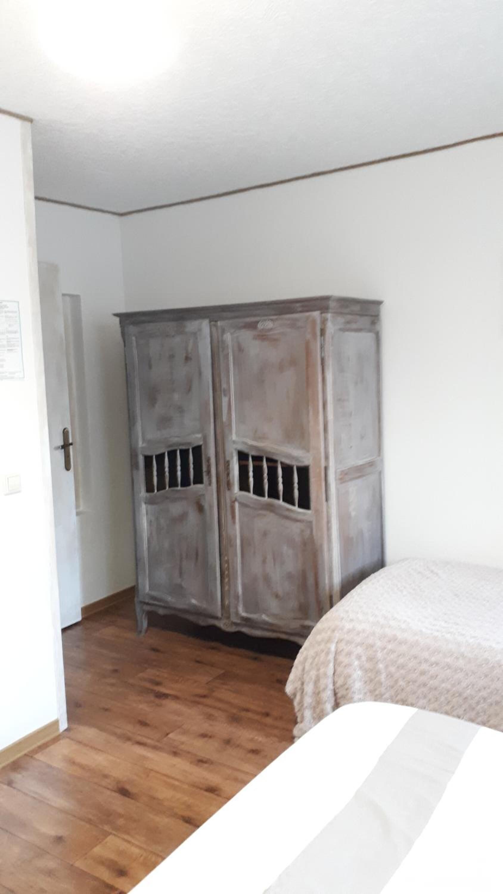 A room with a wooden floor, a white door, and a large wardrobe with a distressed finish.