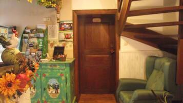 A room with a wooden staircase, a green armchair, a wooden cabinet with a floral design, and a wall-mounted shelf with various items.