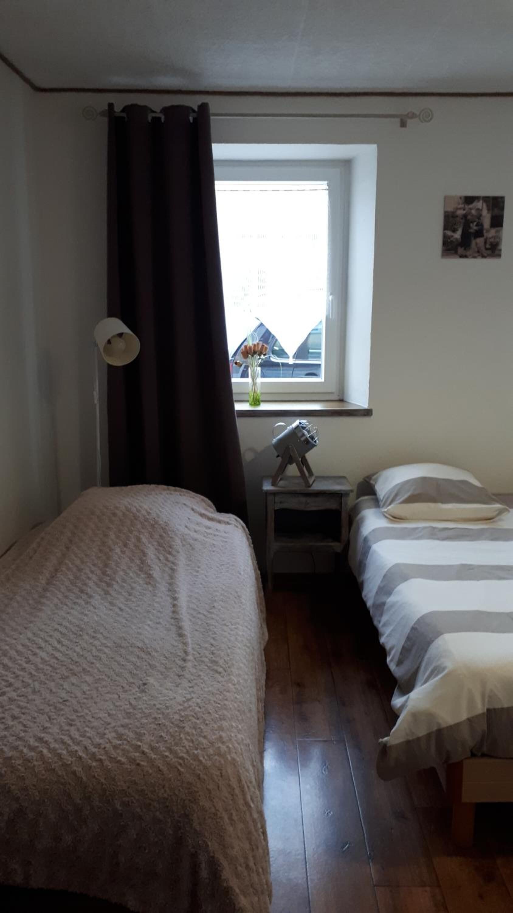 Una habitació petita i acollidora amb dos llits, una finestra amb vista a edificis, una taula petita amb una làmpada i un quadre a la paret.