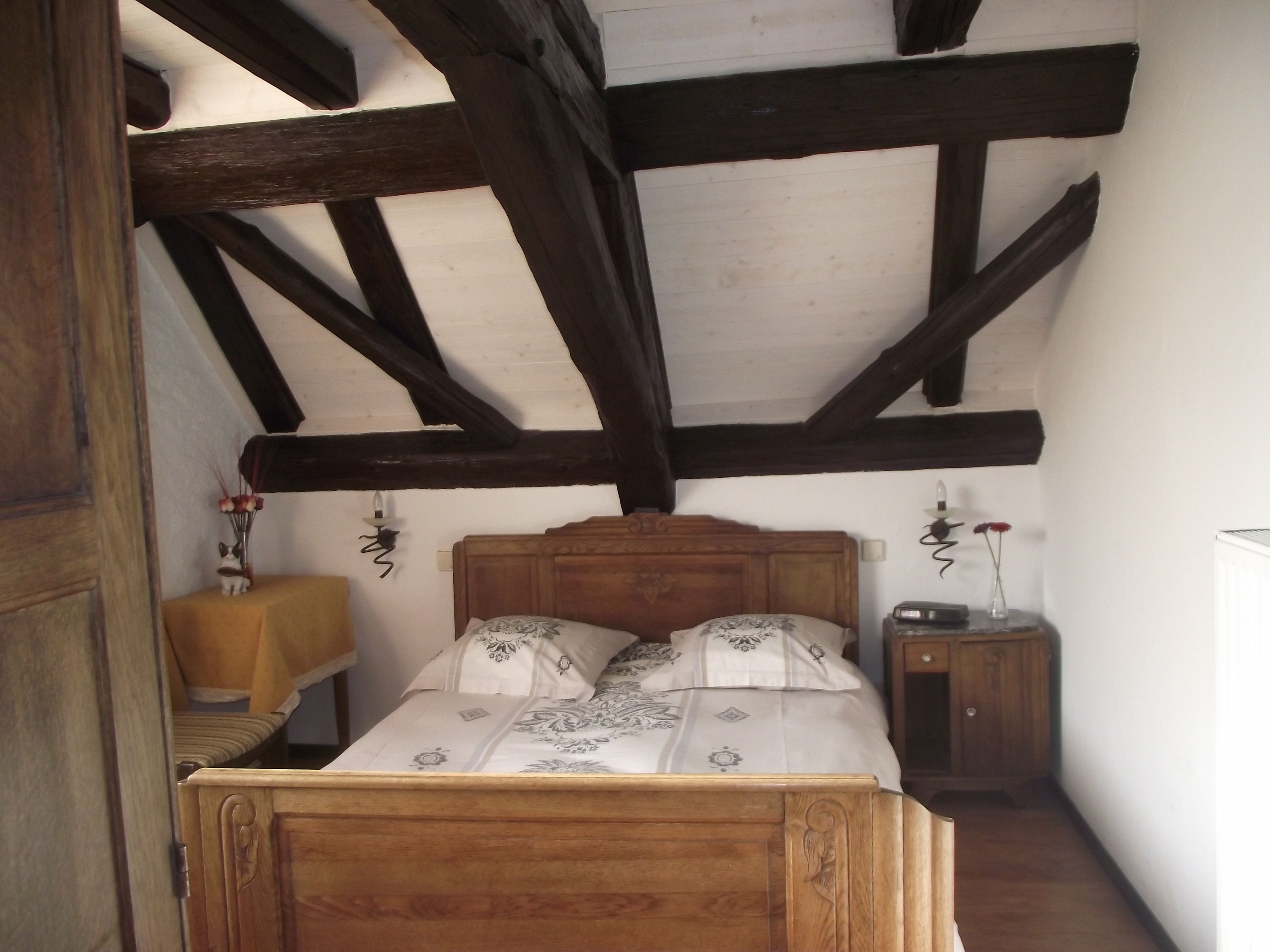 A bedroom with a wooden bed, a nightstand, and a wall-mounted lamp.