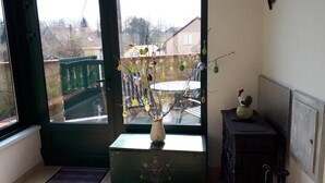 Una habitación con una puerta que da a un balcón, un florero con ramas sobre una mesa y un mueble bajo con un objeto decorativo encima.