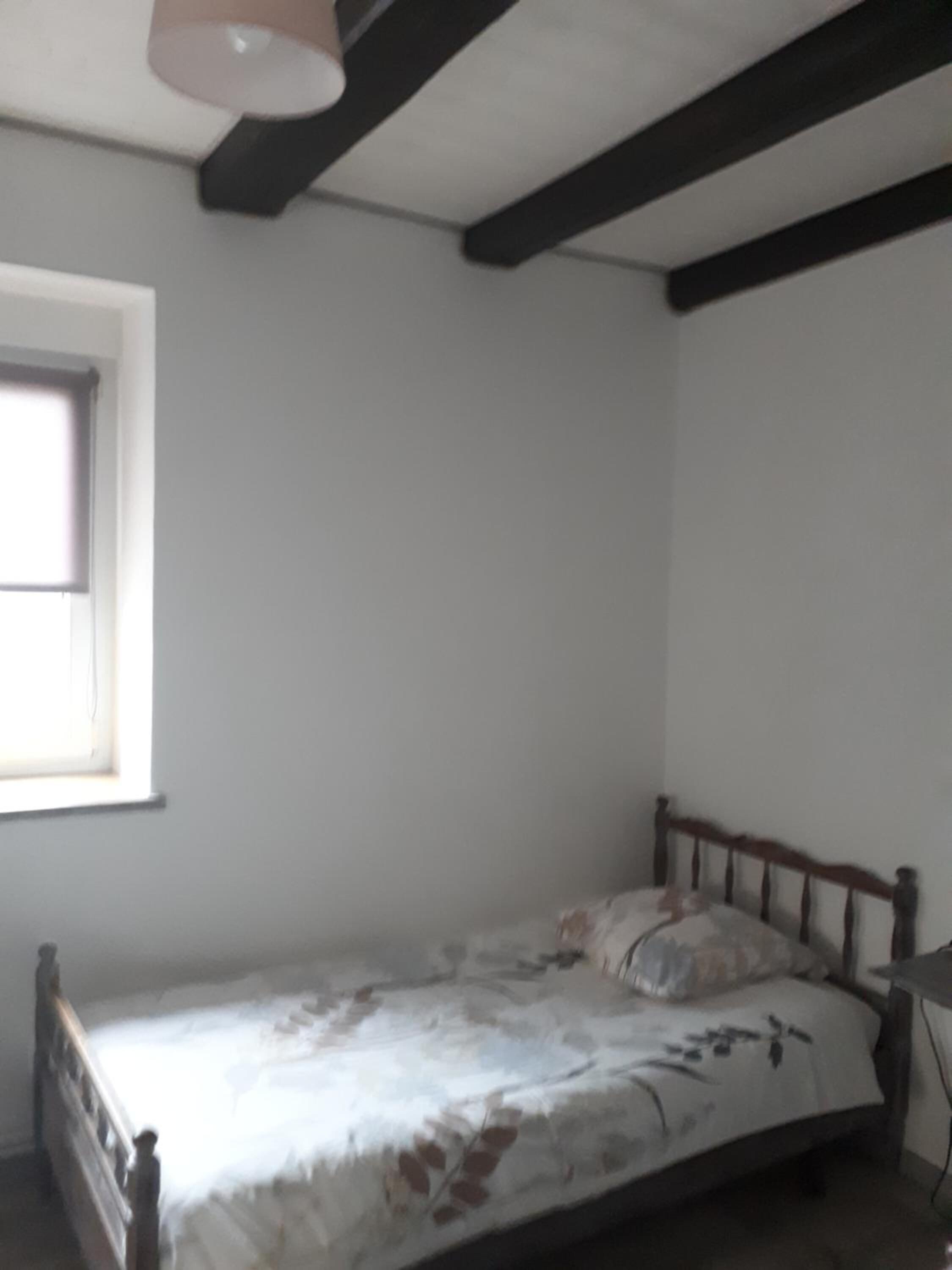 Una habitación pequeña con una cama individual, cabecera de madera, ventana en una pared y techo blanco liso.