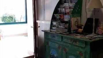 Une pièce avec un meuble vert, une petite table recouverte de papiers, une lampe et une fenêtre donnant sur un paysage.
