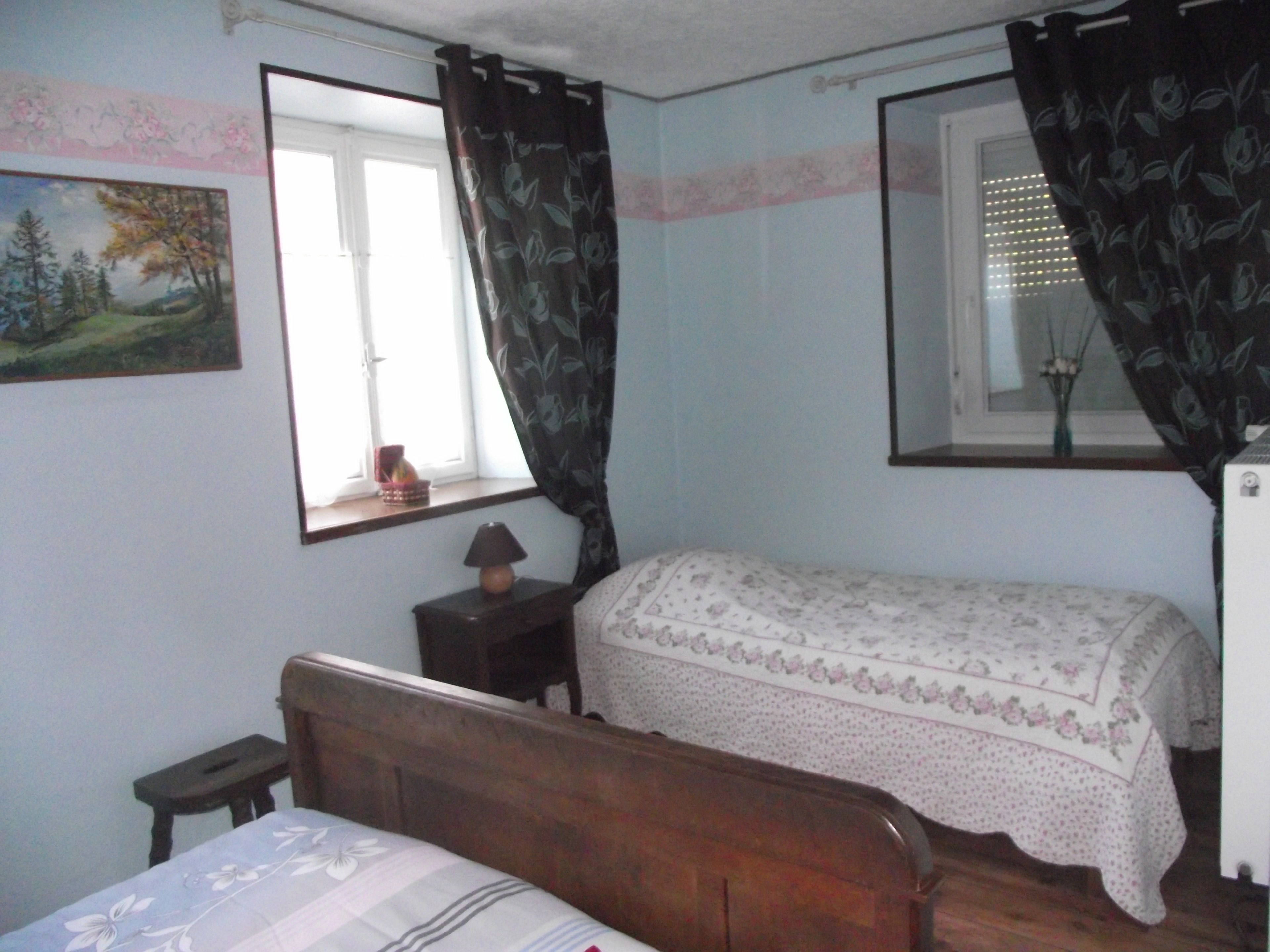 Un dormitorio con una cama de madera, una mesita de noche, una lámpara, una ventana con cortinas y un espejo montado en la pared.