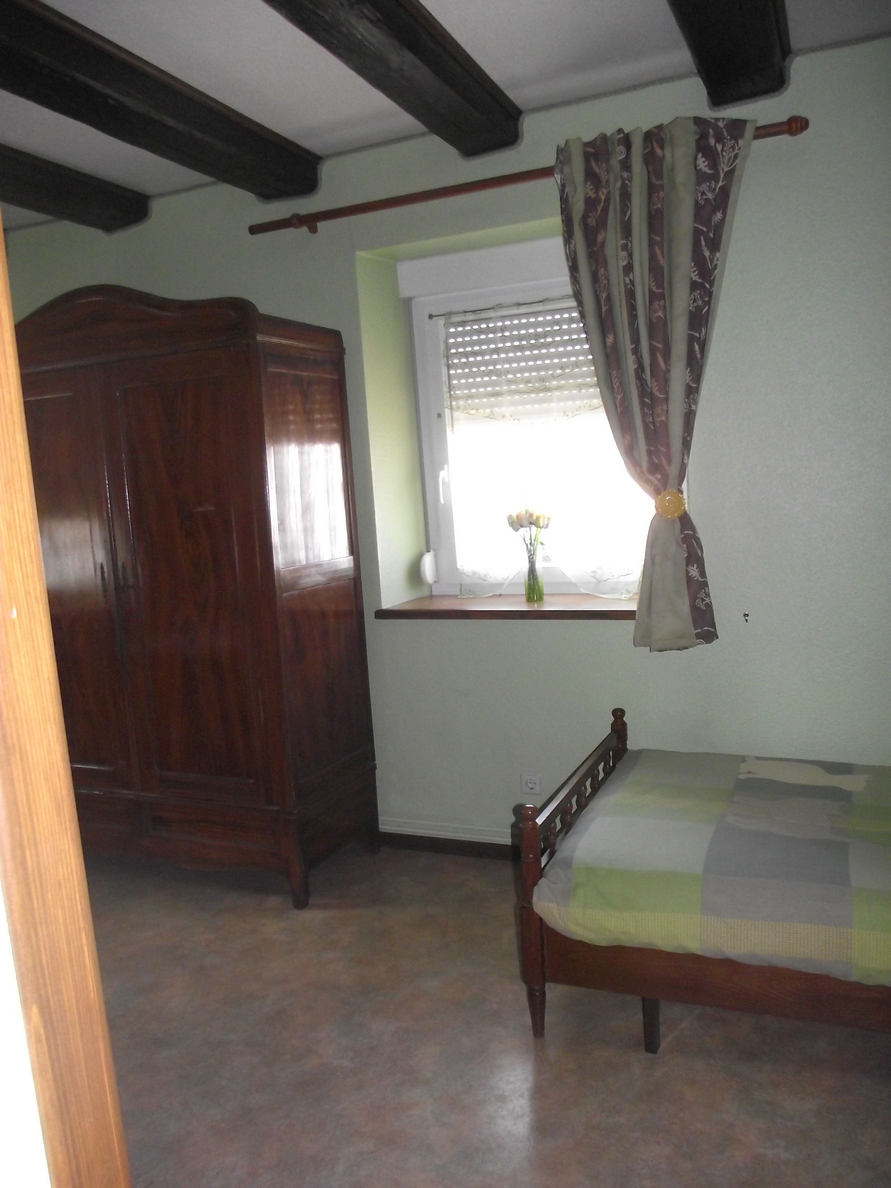 Un dormitorio con una cama de madera, una ventana con cortina y un armario de madera.
