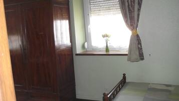 Un dormitorio con una cama de madera, una ventana con cortina y un armario de madera.