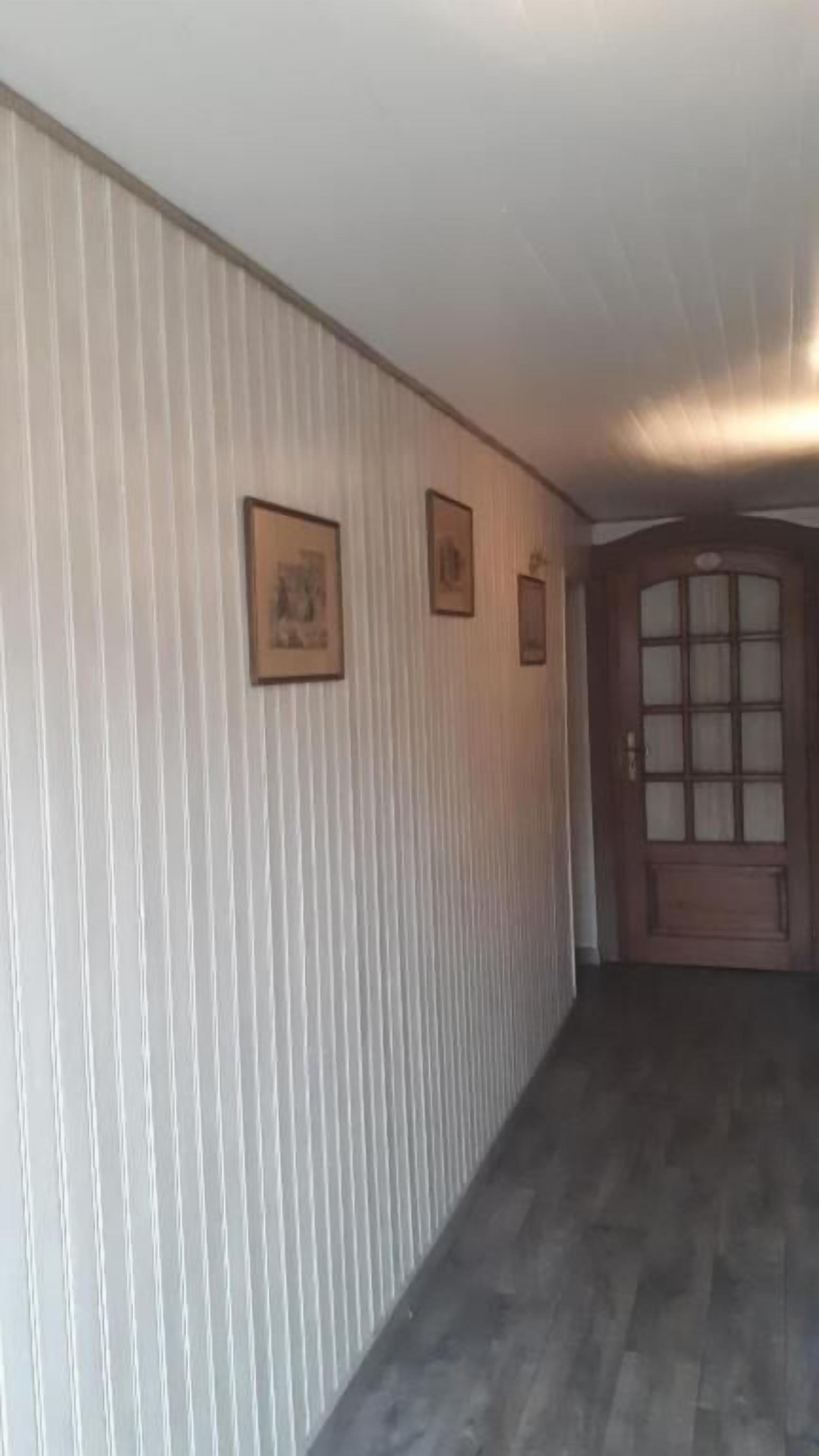 A hallway with vertical striped wallpaper, a wooden door with glass panels, and two framed pictures on the wall.