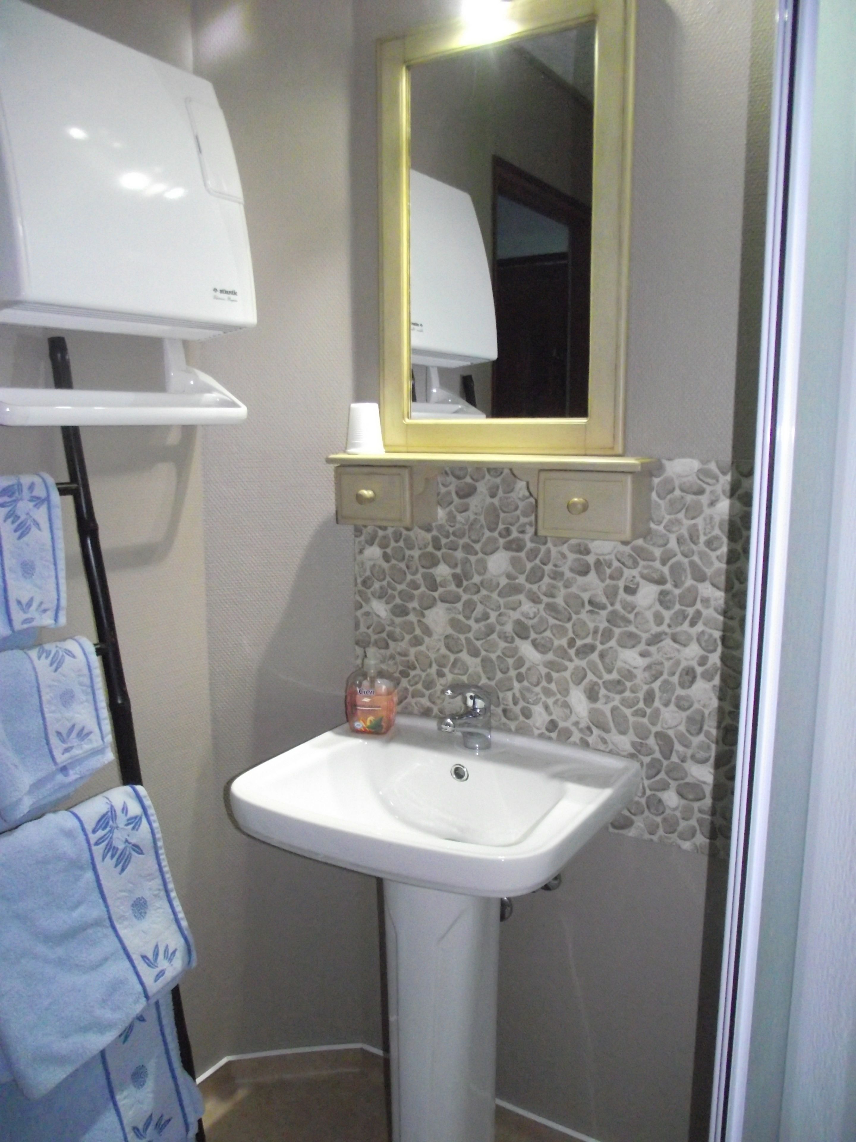 A bathroom with a white sink, a mirror with a gold frame, a towel rack with blue towels, and a soap dispenser.