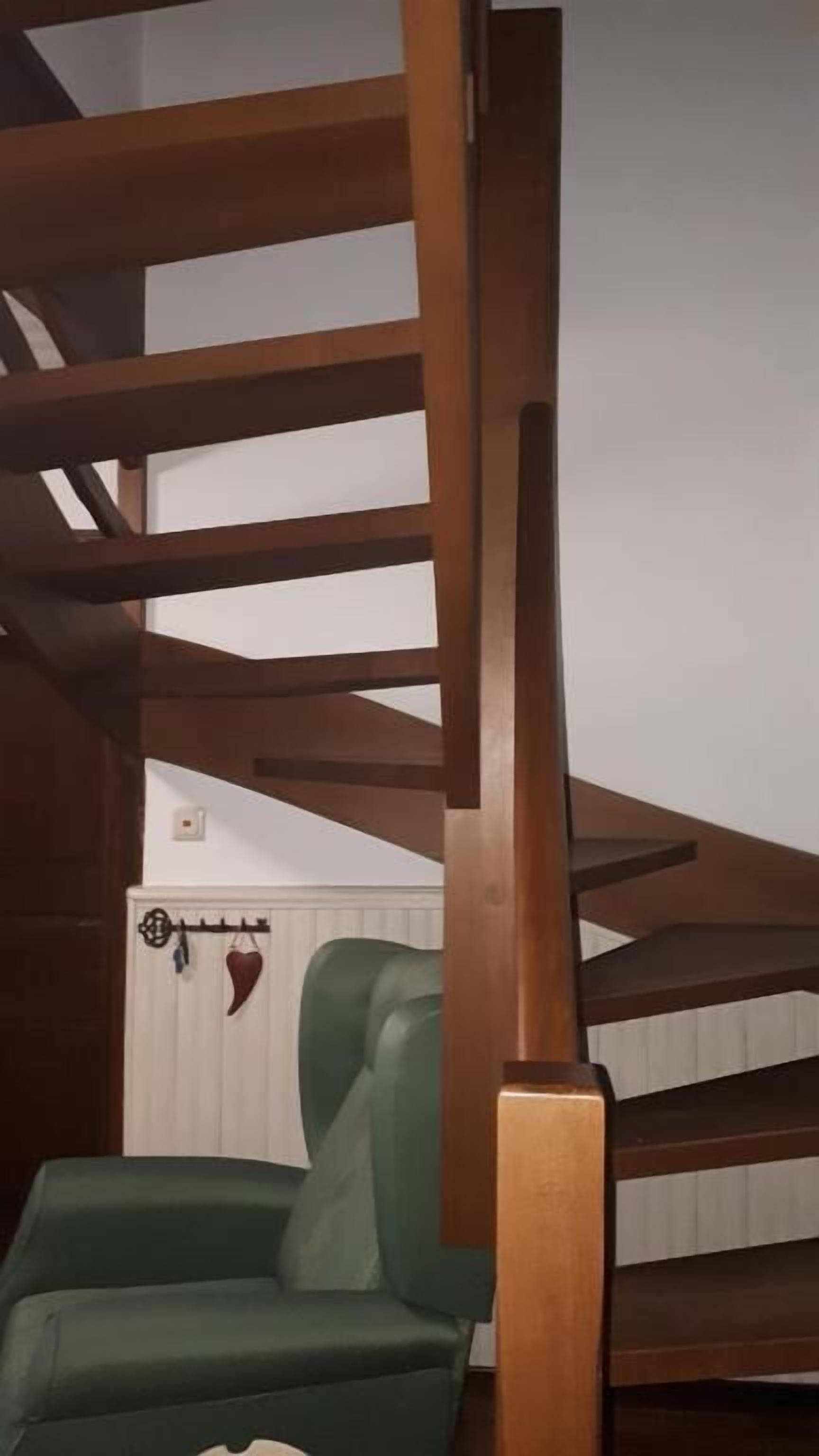 A staircase with wooden railings and a green chair at the bottom.