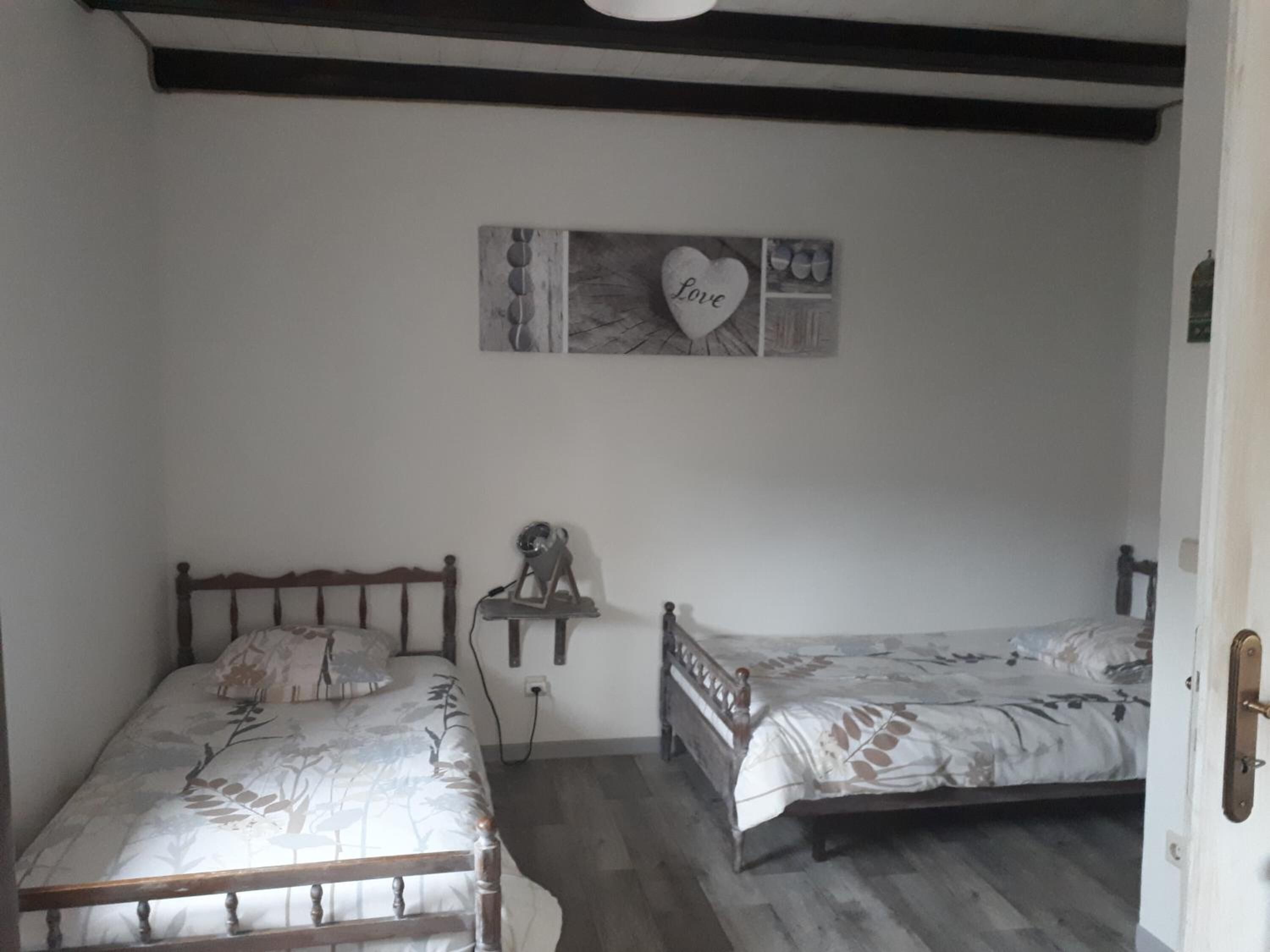 A bedroom with two wooden beds, a wall-mounted shelf, and a 'Love' sign.