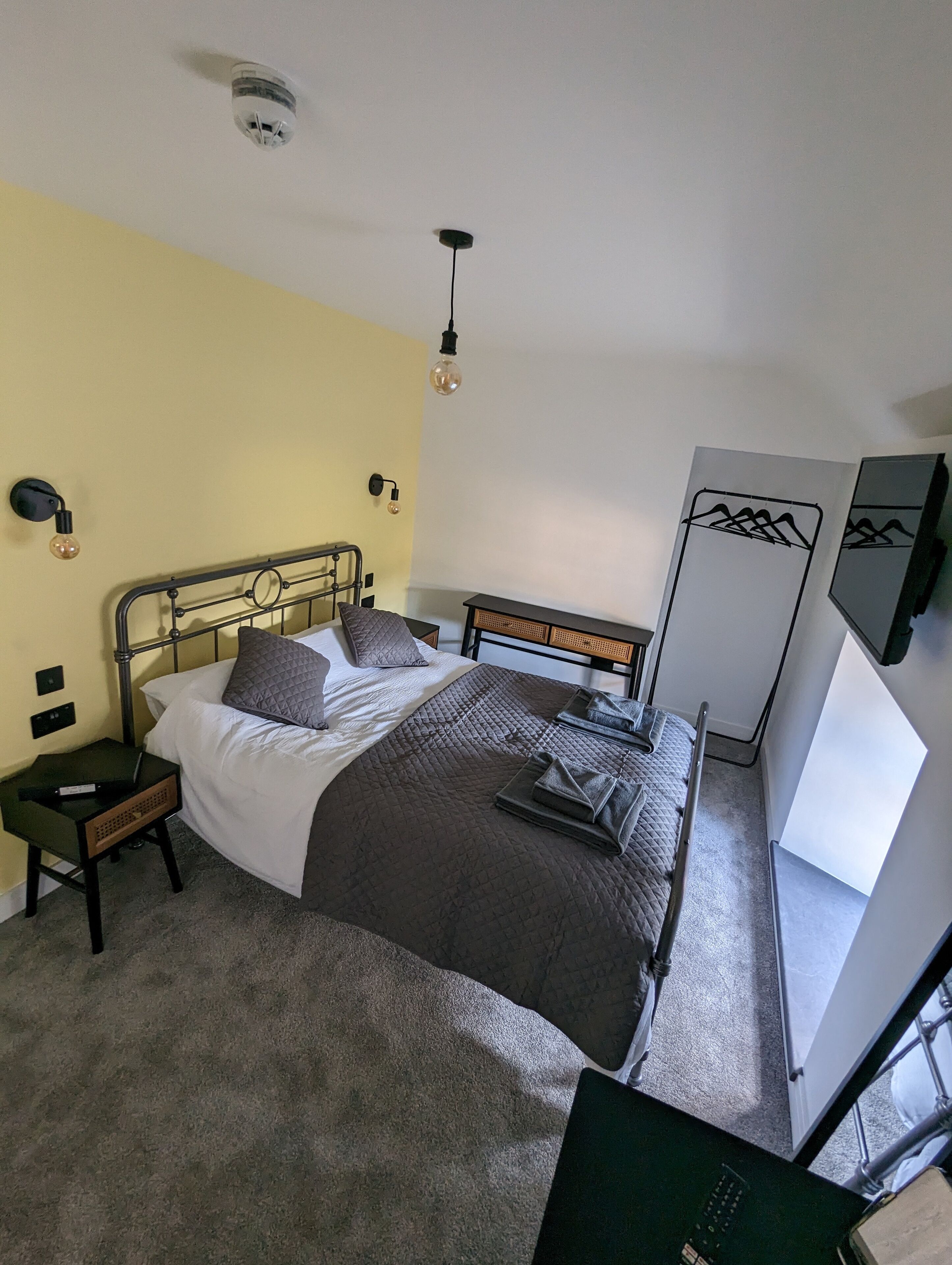 Una camera da letto con un letto, comodini, una TV a muro e una lampada a sospensione.