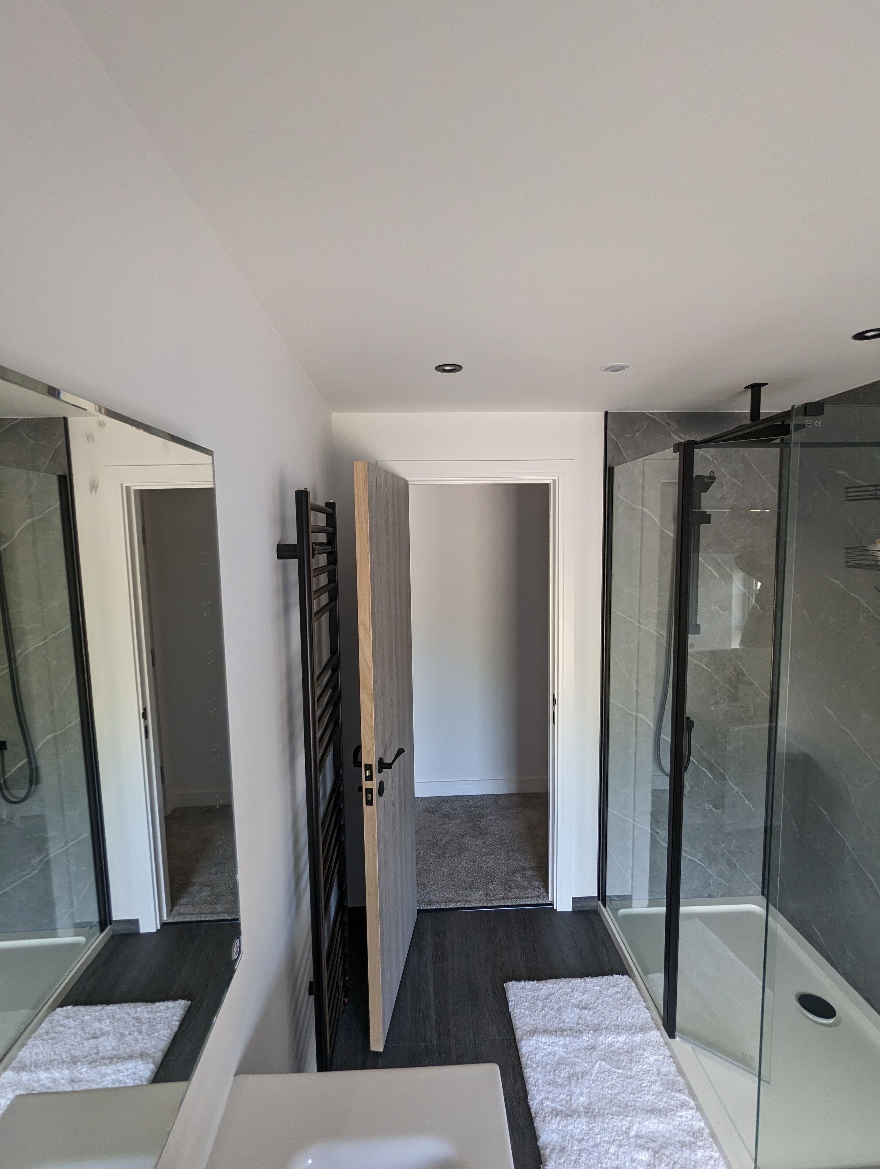 A modern bathroom with a glass shower enclosure, a white bathtub, and a wooden door.