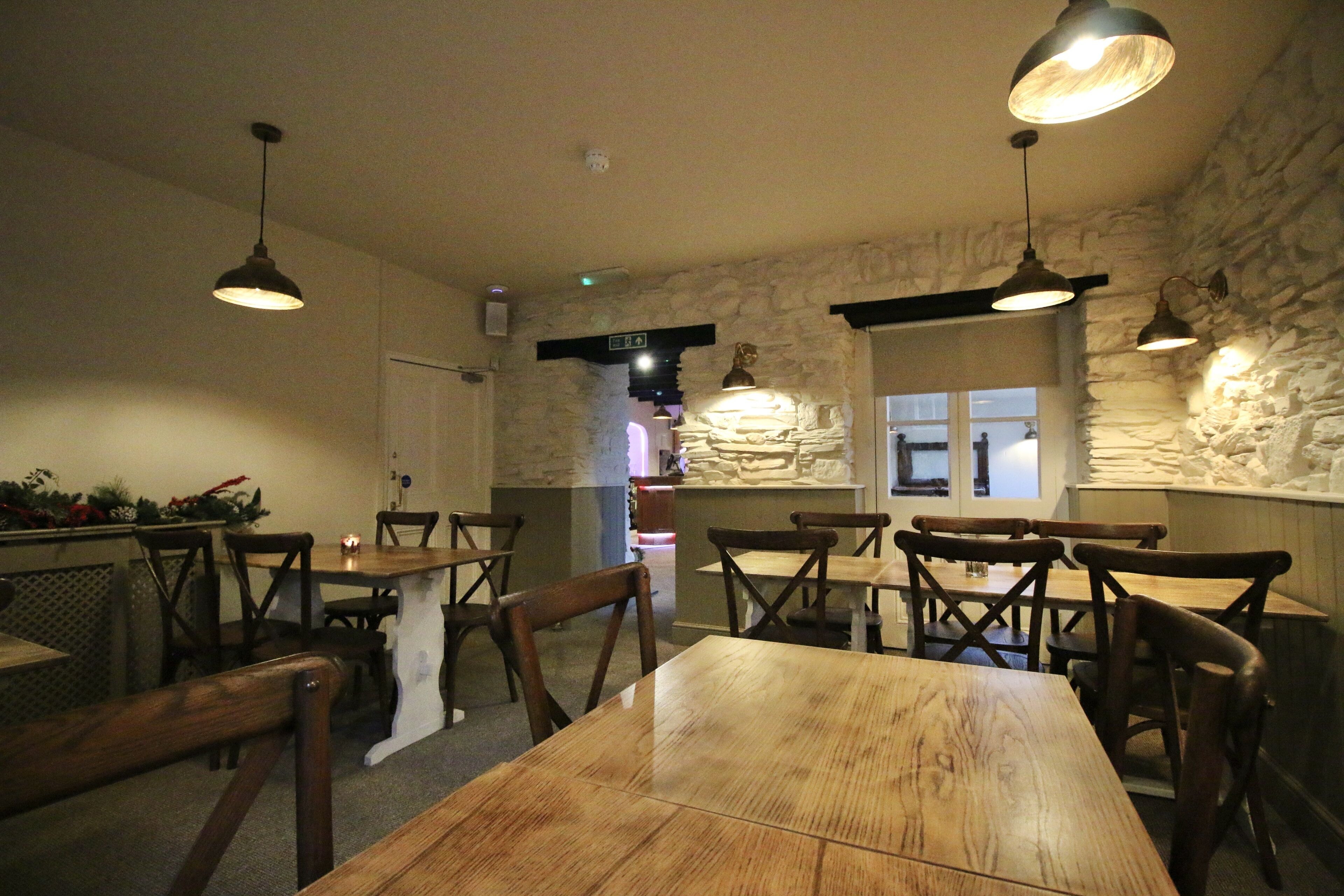 Un restaurante con mesas y sillas de madera, paredes de piedra y lámparas colgantes.