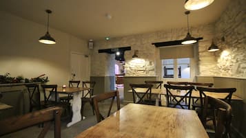 A restaurant with wooden tables and chairs, stone walls, and hanging pendant lights.