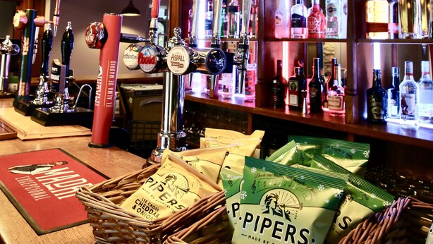 A bar area with multiple beer taps, shelves of liquor bottles, and baskets of Pipers cider vinegar.