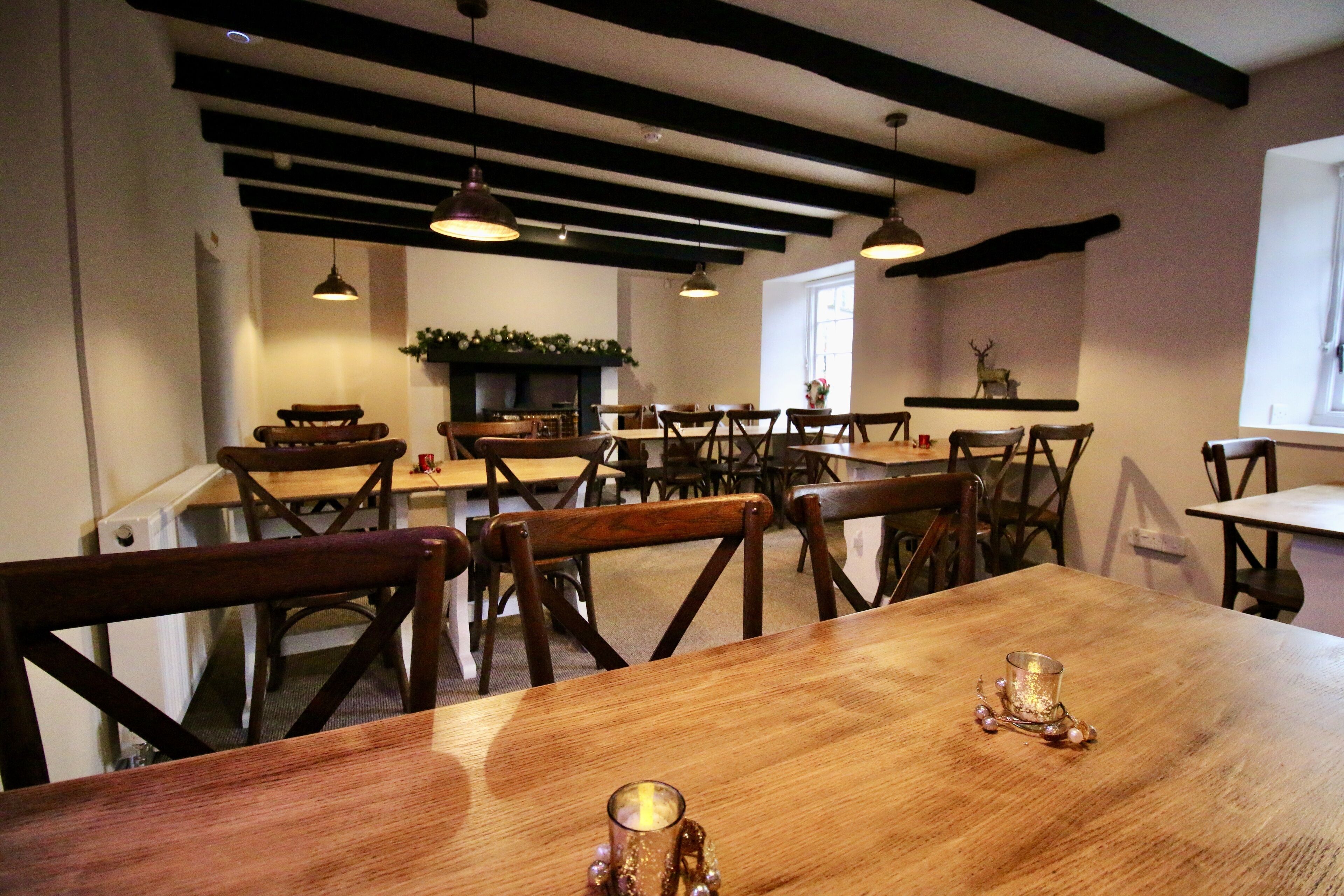 A dining area with wooden tables and chairs, pendant lighting, and a fireplace.