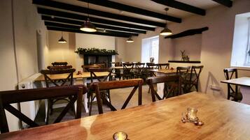 A dining area with wooden tables and chairs, pendant lighting, and a fireplace.