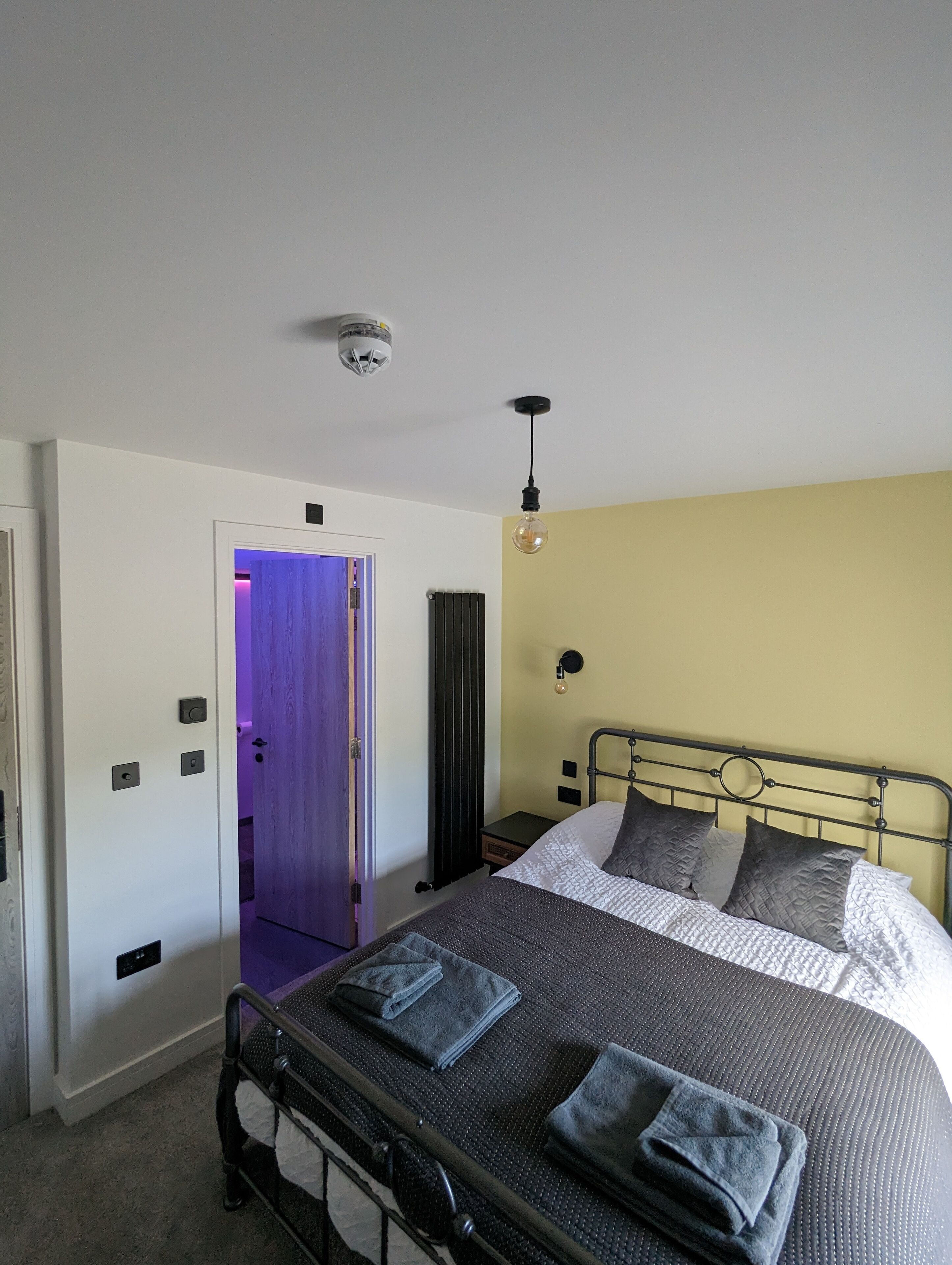 Un dormitorio con cama, mesita de noche, lámpara de pared y puerta que da a otra habitación.