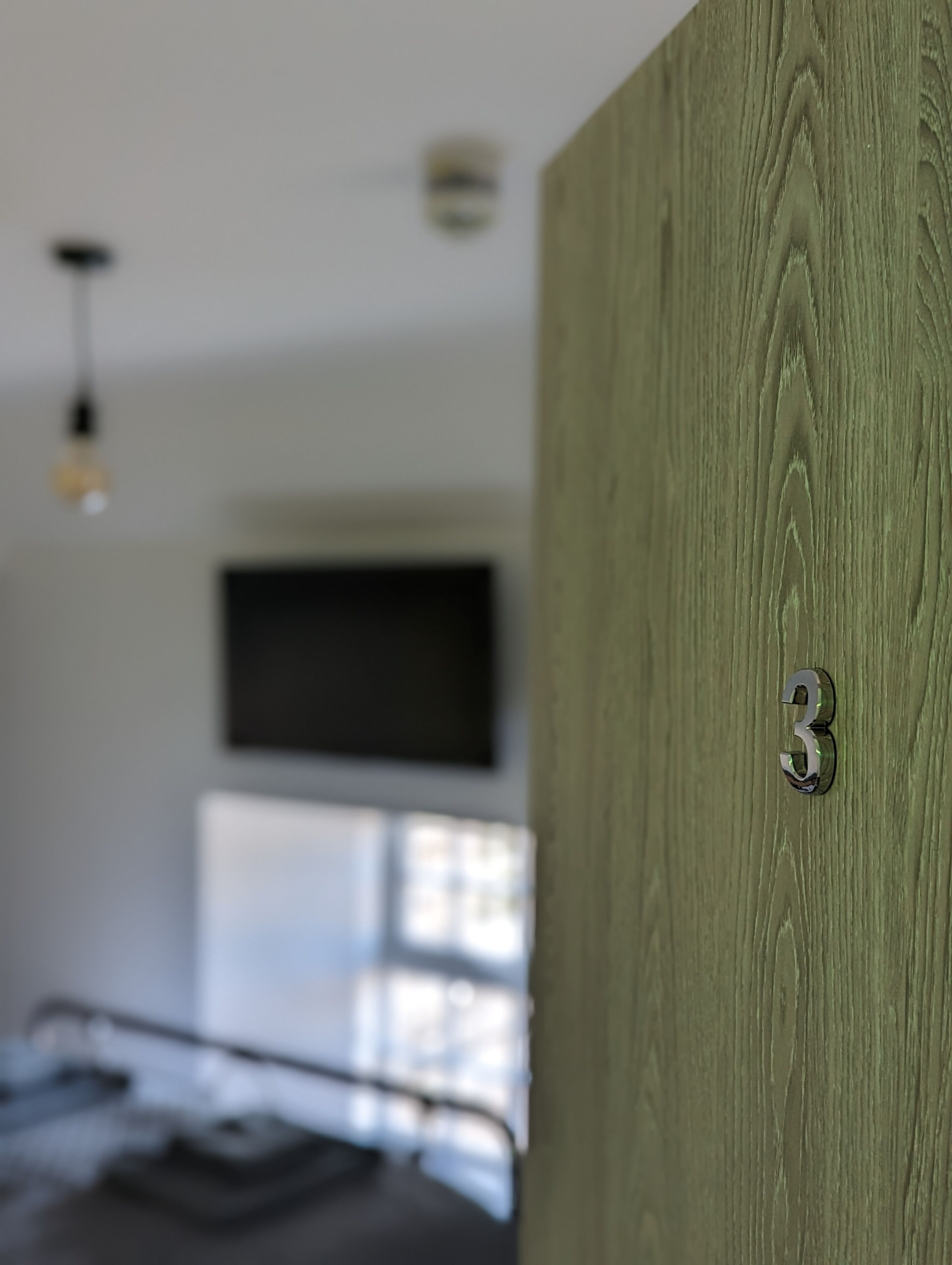 A room with a bed, a mounted TV, and a wooden door with a number '3' on it.
