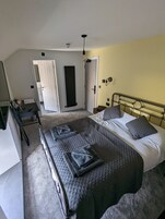 Quarto com cama, escrivaninha e cadeira. Uma porta dá acesso a outro cômodo.