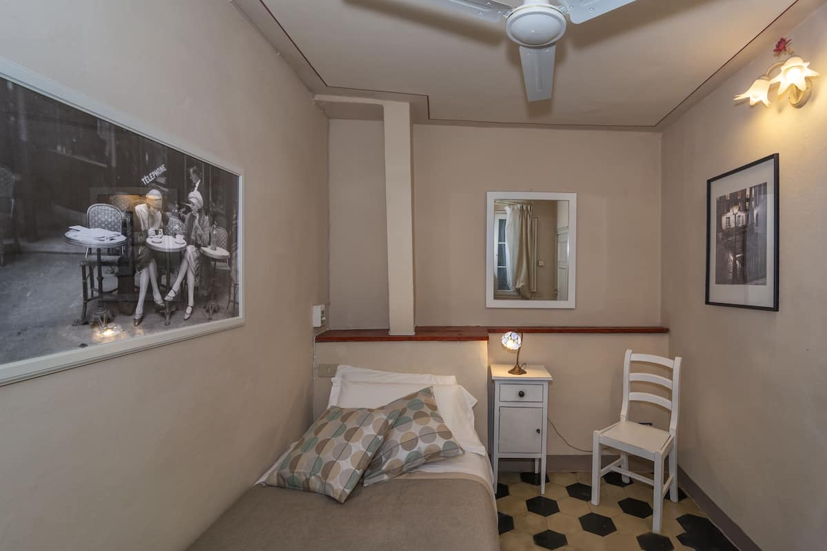 Une chambre à coucher comprenant un lit, une chaise, une table de chevet, un miroir et un luminaire fixé au mur.
