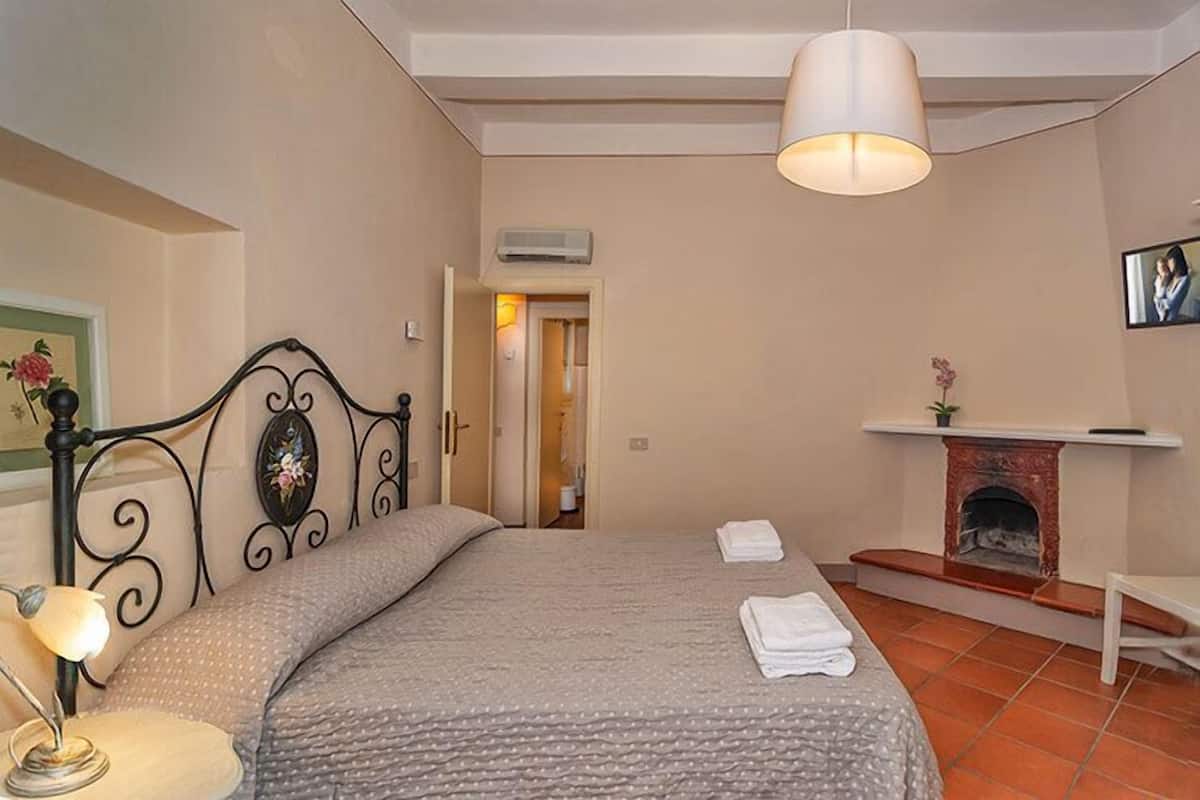 Une chambre à coucher avec un lit, une lampe de chevet, une cheminée et un téléviseur fixé au mur.