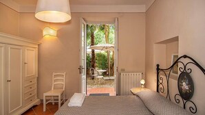A bedroom with a bed, a chair, a wardrobe, a door leading to an outdoor patio with a table and umbrella. - Corte Meraviglia - Relais (Lucca)