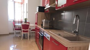 A compact kitchen with red cabinets, a stainless steel sink, and a small dining area with a table and chairs. - Pula Antic Rooms in Center- Adults only (Pula)