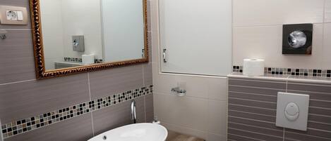 Un baño con un lavamanos blanco, un espejo con marco dorado y un dispensador de papel higiénico.