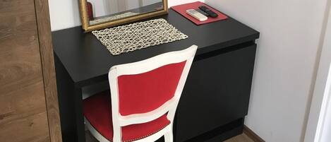 Un espace de travail compact avec un bureau noir, une chaise rouge, un miroir à cadre doré et un tapis rouge.