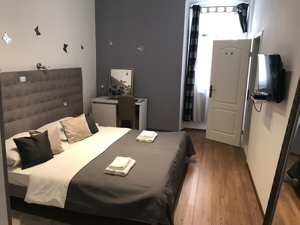 Quarto com cama, escrivaninha, cadeira, televisão e porta.