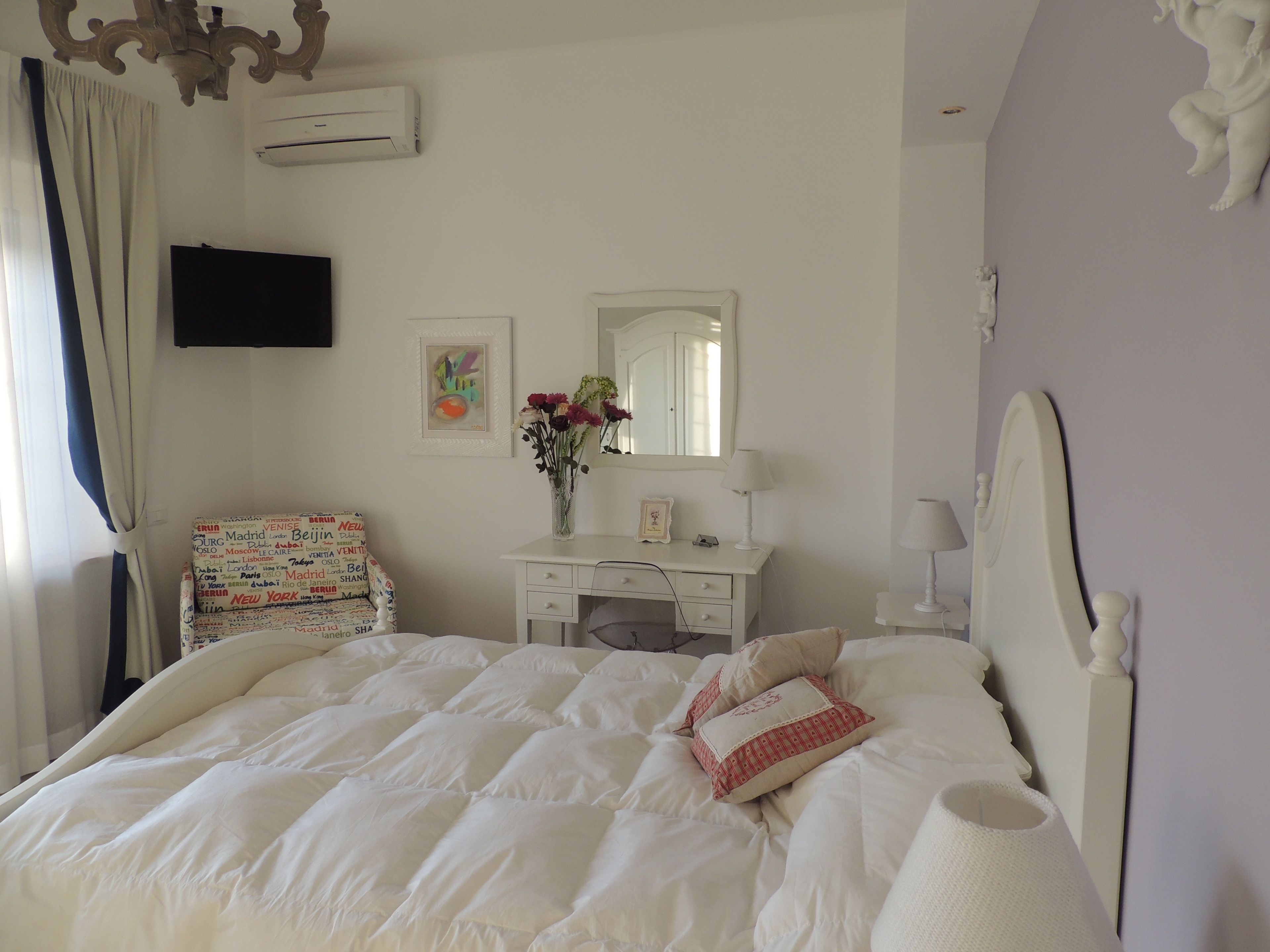 A bedroom with a bed, a dresser, a mirror, a TV, and a wall with a decorative piece.