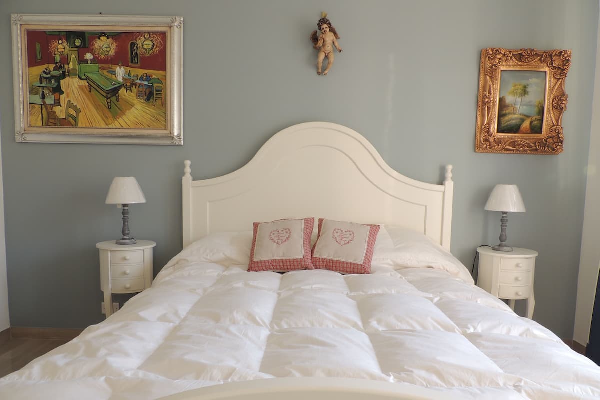 A neatly made bed with white bedding and two heart-shaped pillows, flanked by two bedside tables with lamps, against a light blue wall.