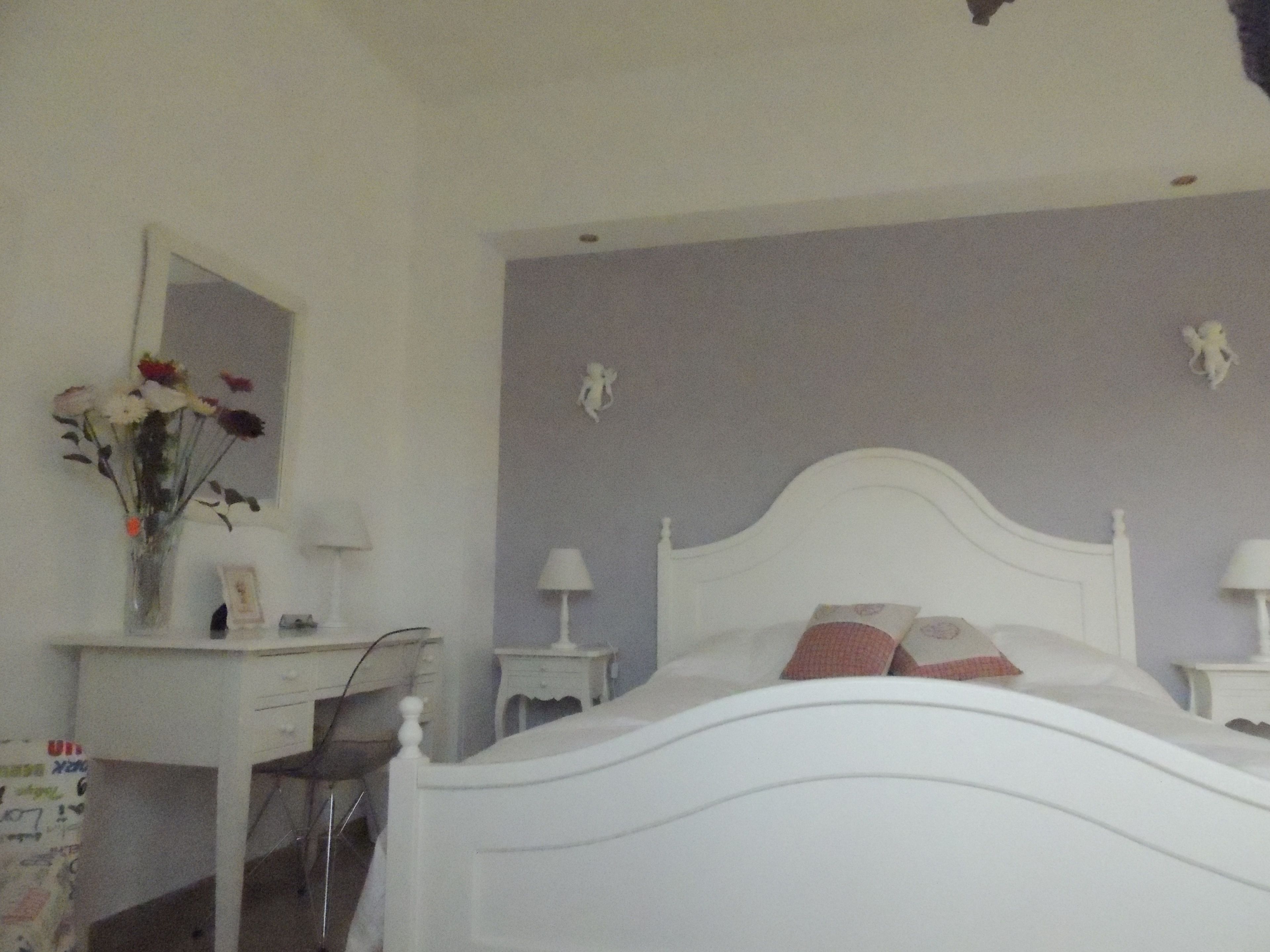 Een slaapkamer met een wit bed, een bureau met een spiegel en een vaas met bloemen.