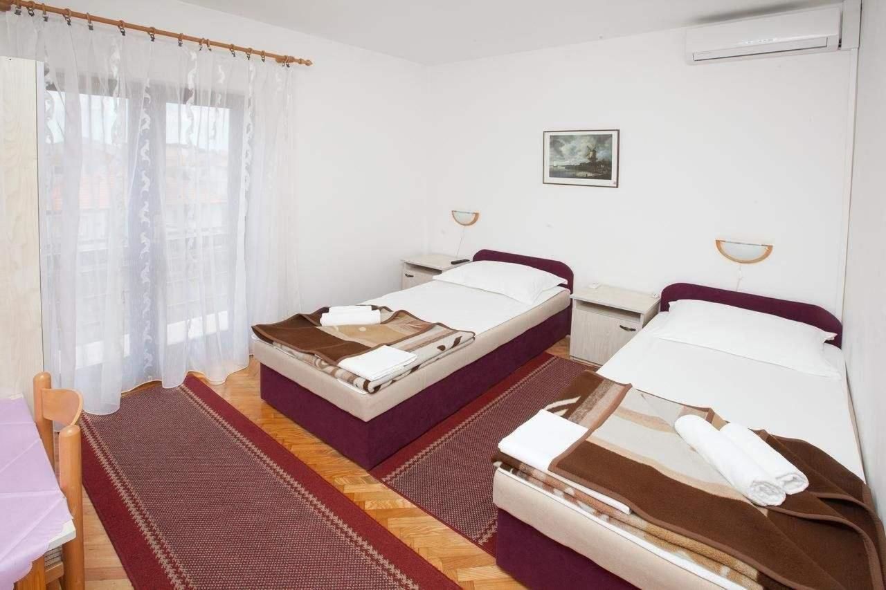 A double room with two beds, a small table, a chair, and a window with sheer curtains.