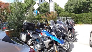 Una fila de motocicletas estacionadas en un estacionamiento con un cartel que indica servicios como habitaciones, departamentos y cámaras de seguridad.